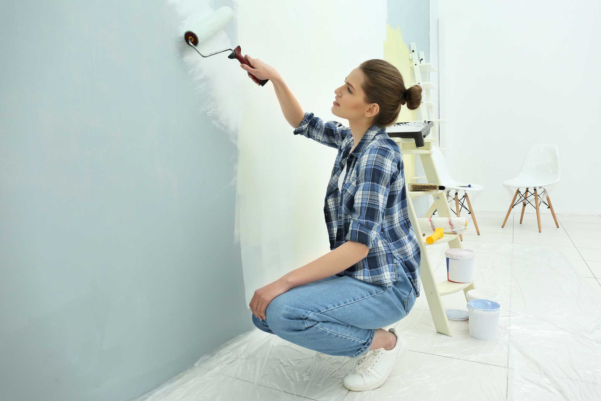 Beautiful young woman painting wall in room
