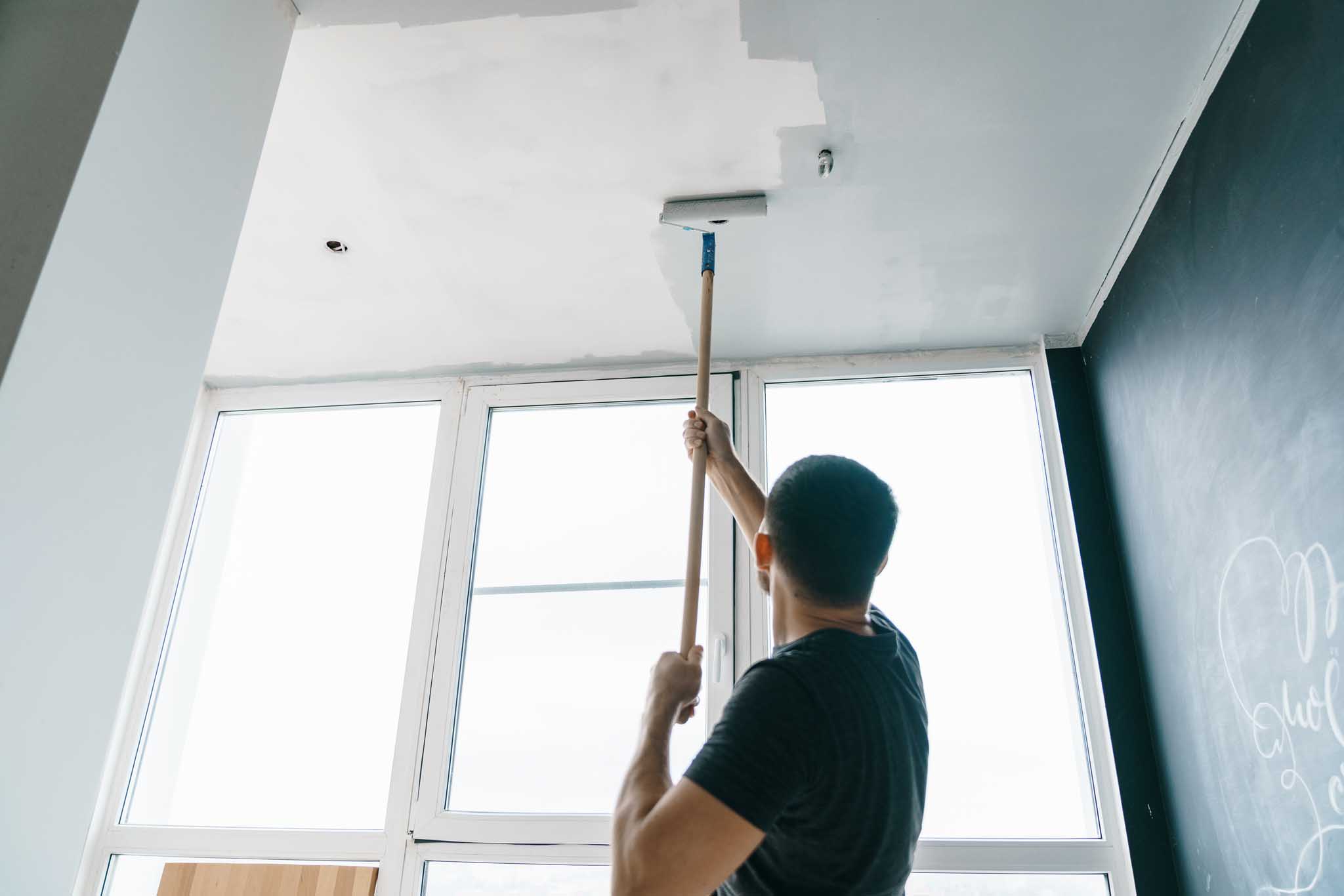 The man paints the walls and the ceiling in gray color, standing