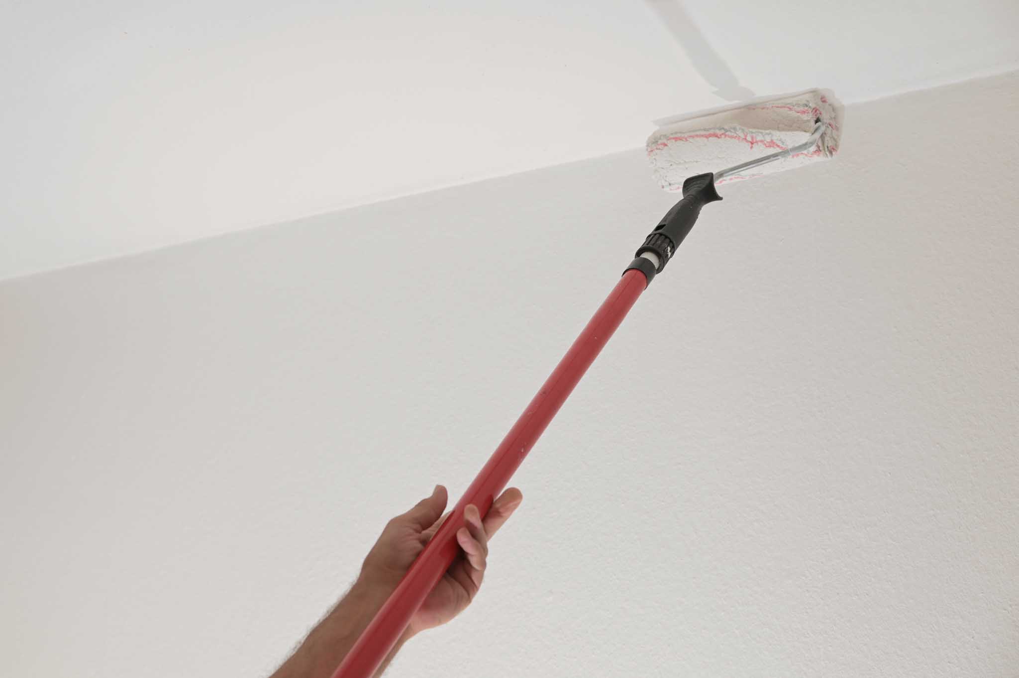 Hand of a man holding a paint roller on a long telescopic pole t