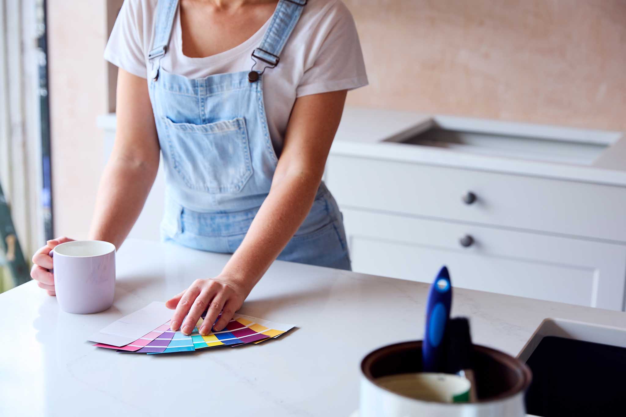 Close Up Of Woman Renovating Kitchen At Home Looking At Paint Sw